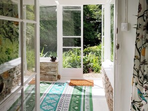 A room with a view of a garden through a glass door, a stone wall, and a patterned rug on the floor. - 3 bedroom accommodation in Kingsbrisge (Kingsbrisge)