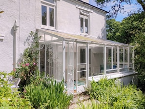 A house with a conservatory, a white exterior, and a garden with various plants. - 3 bedroom accommodation in Kingsbrisge (Kingsbrisge)