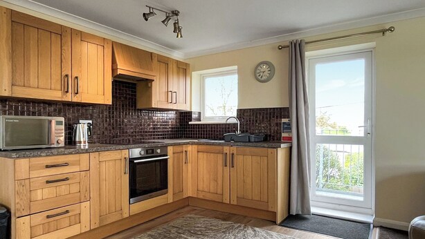 A kitchen with wooden cabinets, a microwave, an oven, a sink, and a window with a view. - 3 bedroom accommodation in Trerulefoot (Trerulefoot)