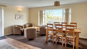 A dining area with a wooden table and chairs, a sofa, a rug, and a window with a view. - 3 bedroom accommodation in Trerulefoot (Trerulefoot)