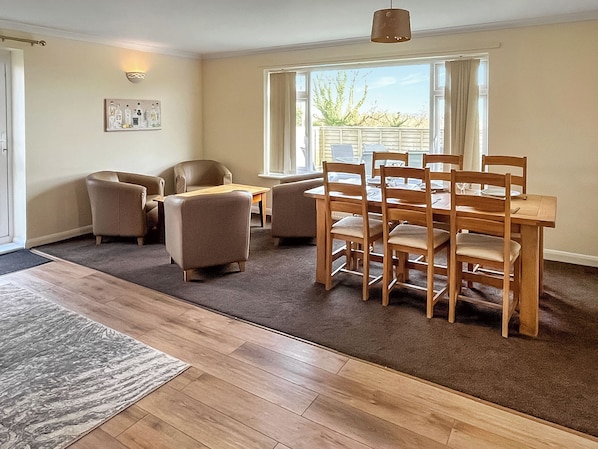 A dining area with a wooden table and chairs, a sofa, a rug, and a window with a view.