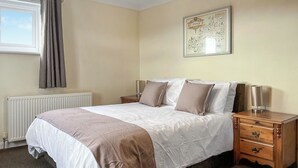 A bedroom with a bed, bedside tables, a radiator, a window with curtains, and a framed picture on the wall. - 3 bedroom accommodation in Trerulefoot (Trerulefoot)