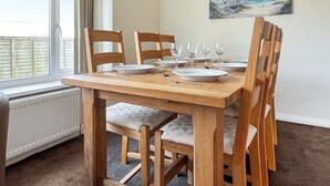A dining area with a wooden table and chairs, a painting on the wall, and a view of the sea through a window. - 3 bedroom accommodation in Trerulefoot (Trerulefoot)