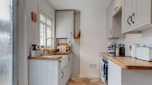 Een compacte keuken met witte kasten, een houten aanrecht, een spoelbak en een ingebouwde oven.