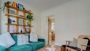 Een woonkamer met een blauwgroene bank, een houten salontafel, een boekenkast en een eethoek op de achtergrond.