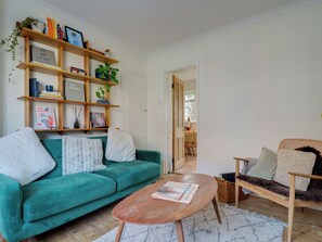 Un salon avec un canapé de couleur turquoise, une table basse en bois, une bibliothèque et, au fond, un coin repas.