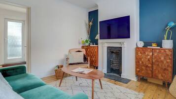 A living room with a teal sofa, a wooden coffee table, a fireplace, and a cabinet with geometric patterns.