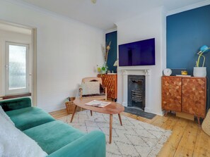 A living room with a teal sofa, a wooden coffee table, a fireplace, and a cabinet with geometric patterns.