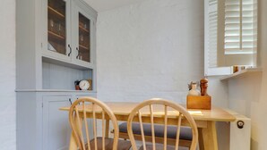 Een keuken met een houten tafel en twee stoelen, een kast met glazen deuren en een klok aan de muur.