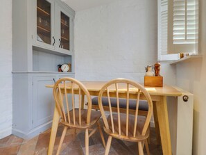 Una cocina con una mesa de madera y dos sillas, un armario con puertas de cristal y un reloj en la pared.