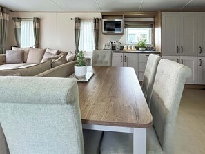A compact living space with a sofa, a dining table, and kitchen cabinets. - Beaumont Elite Lodge (Wemyss Bay)