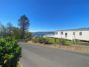 A mobile home with a white exterior, a deck, and a view of a body of water. - Beaumont Elite Lodge (Wemyss Bay)