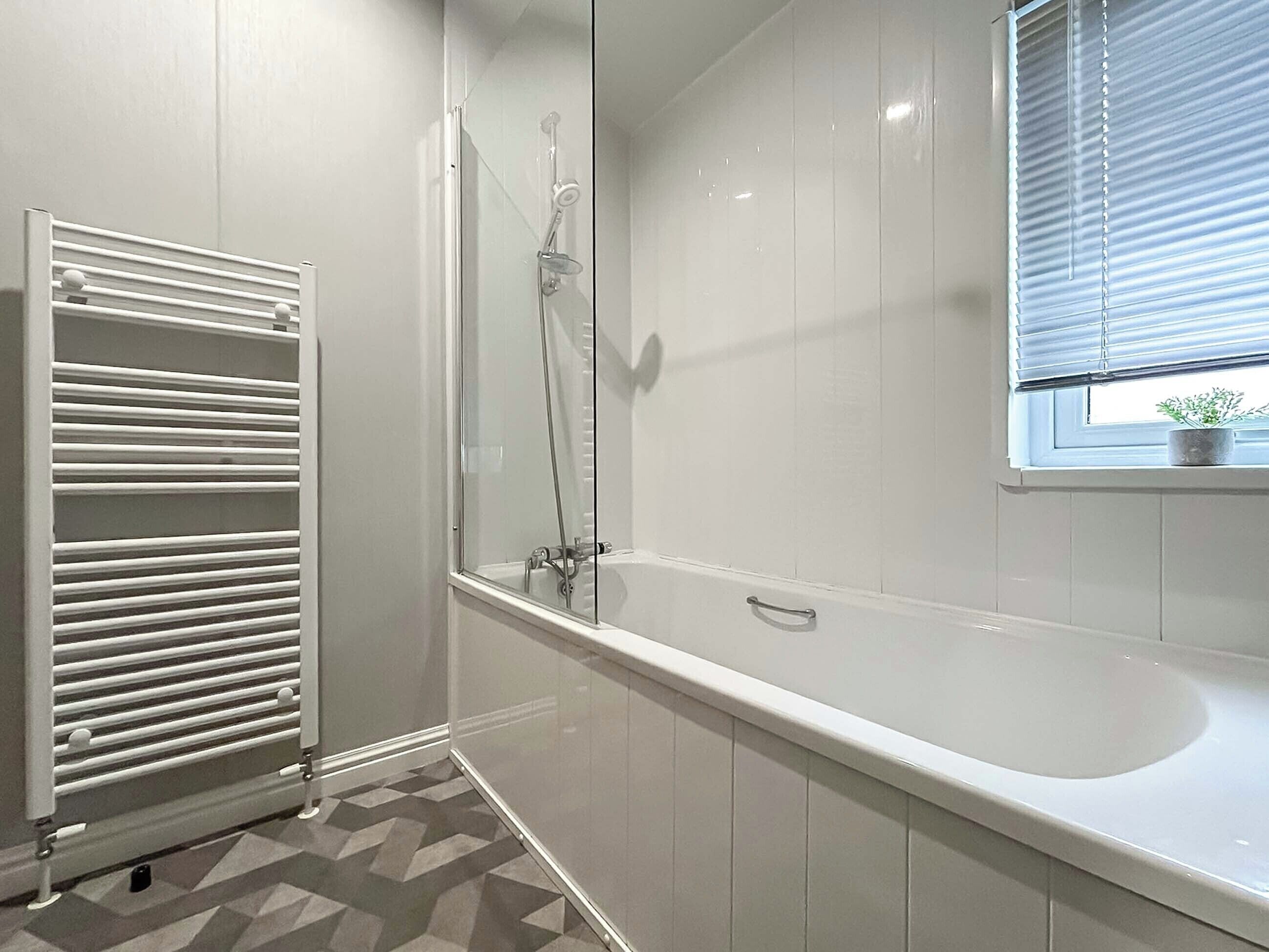 Un bagno moderno con vasca, cabina doccia in vetro, termosifone e finestra con persiane.