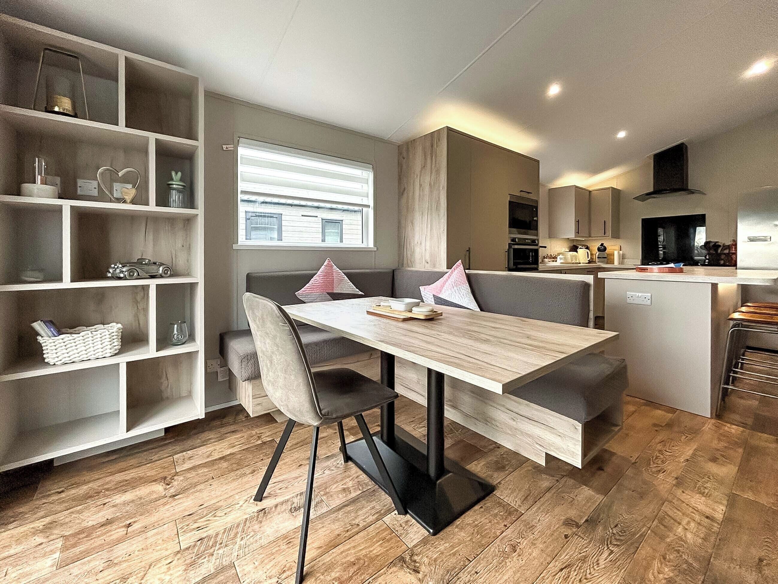 A modern kitchen with a dining area, wooden flooring, and built-in shelving.