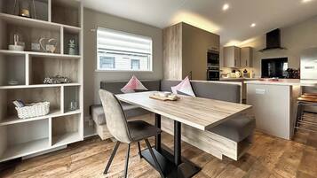 A modern kitchen with a dining area, wooden flooring, and built-in shelving.