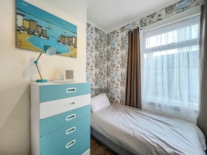 Une chambre à coucher avec un lit, une commode, une lampe de bureau, un tableau et une fenêtre avec des rideaux.