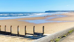 Ein Strand mit einer Holzpromenade, die zum Ufer führt, feinem Sand und dem Meer im Hintergrund.