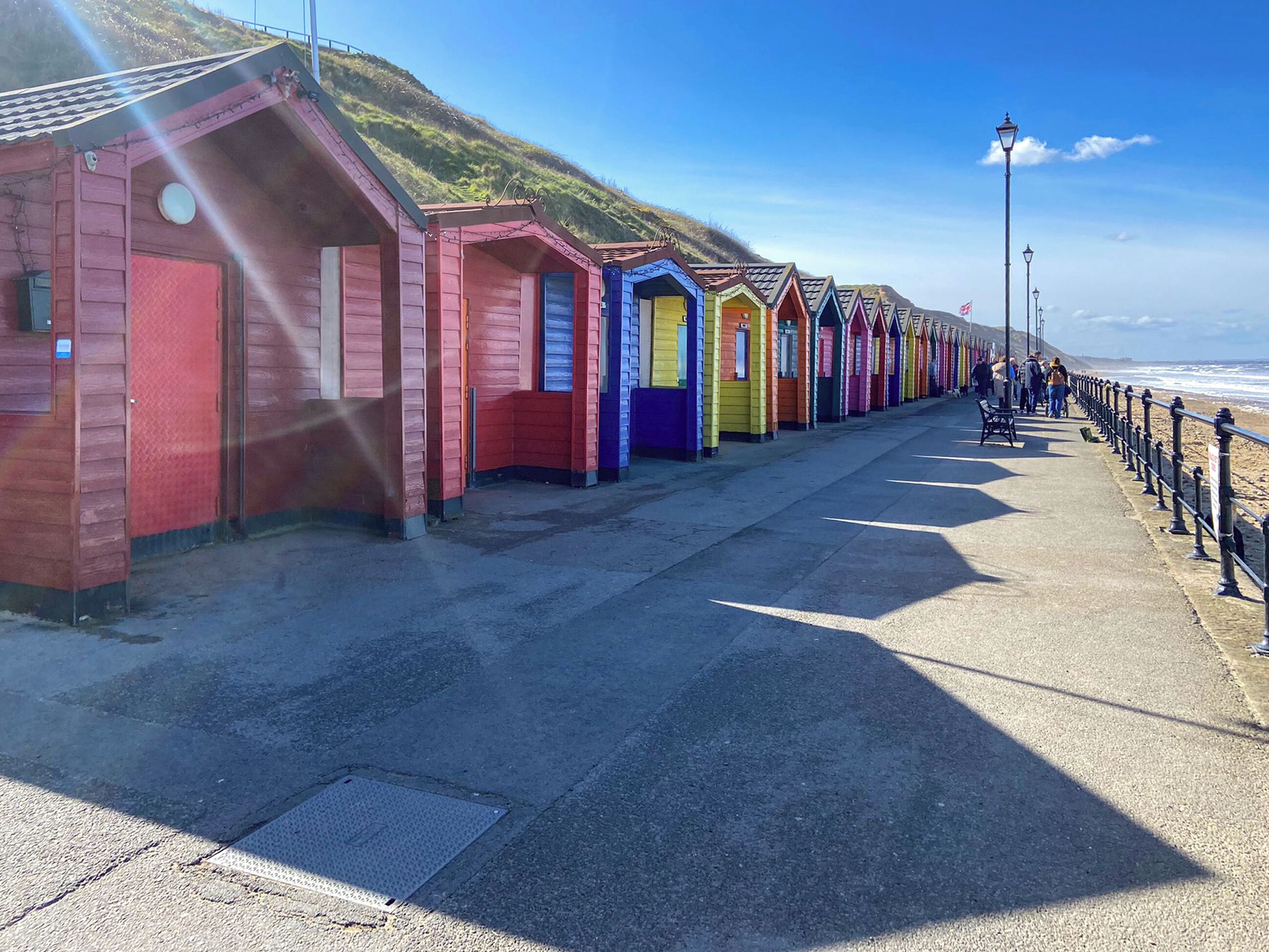 Una hilera de cabañas de playa coloridas a lo largo de un paseo marítimo, bajo un cielo despejado.