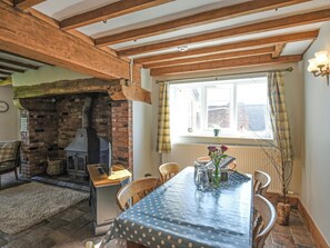 A dining area with a brick fireplace, wooden beams, a table with a polka dot tablecloth, and a window with curtains. - 3 bedroom accommodation in Malpas (Malpas)