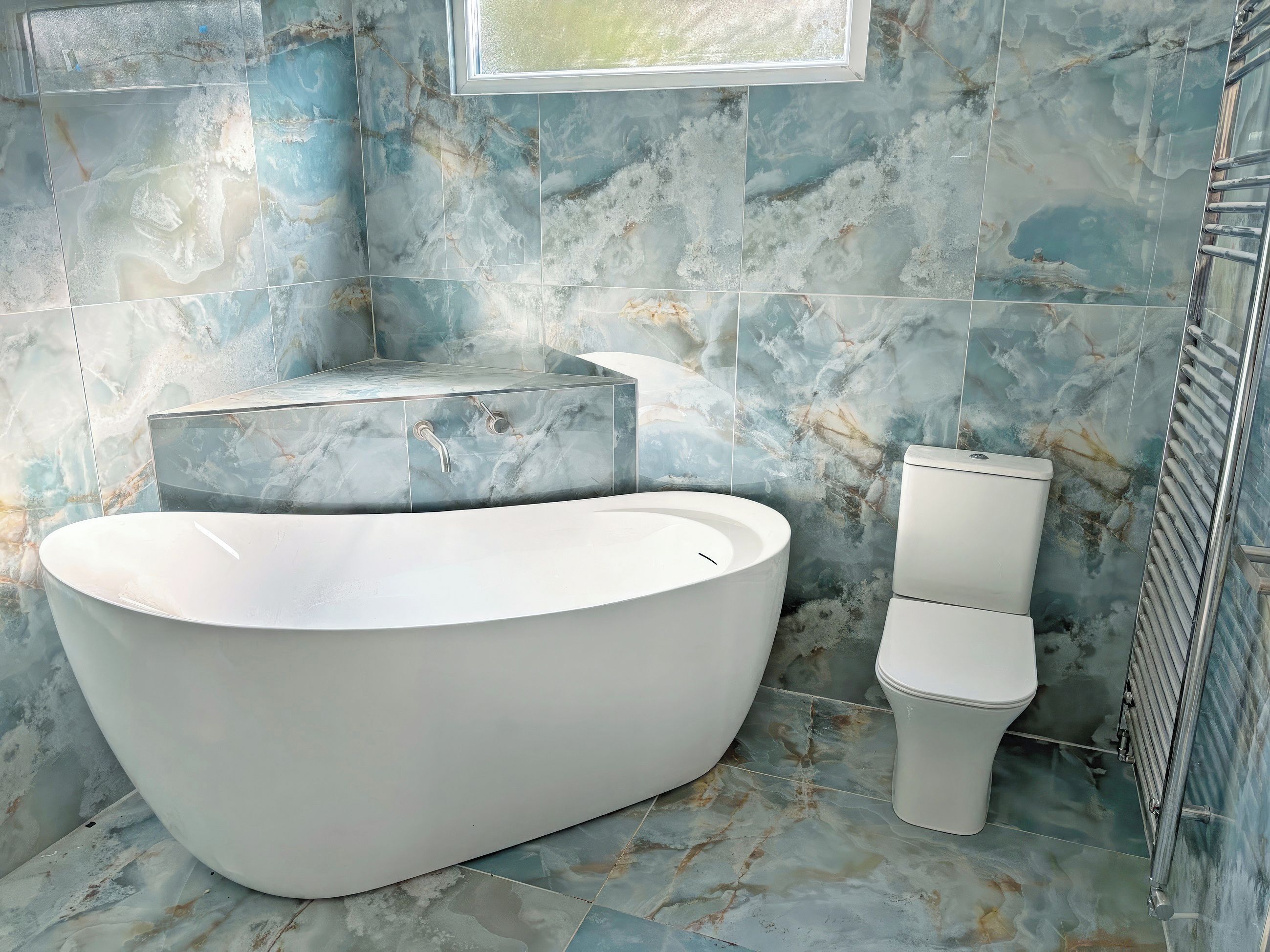 Une salle de bain avec une baignoire sur pieds, des toilettes et des murs décorés d’un motif imitant le marbre.