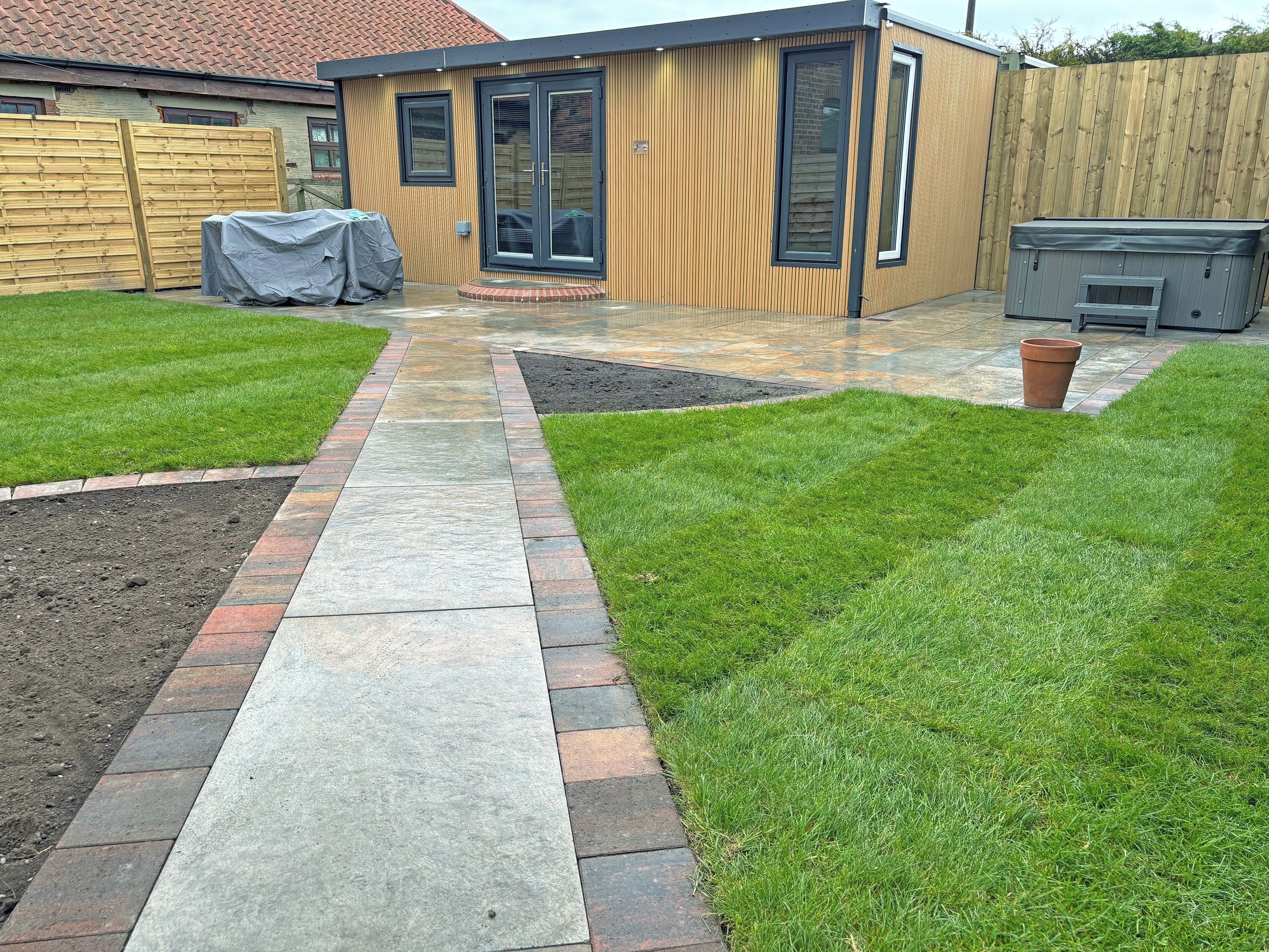 A modern house with a patio, a wooden fence, and a garden.