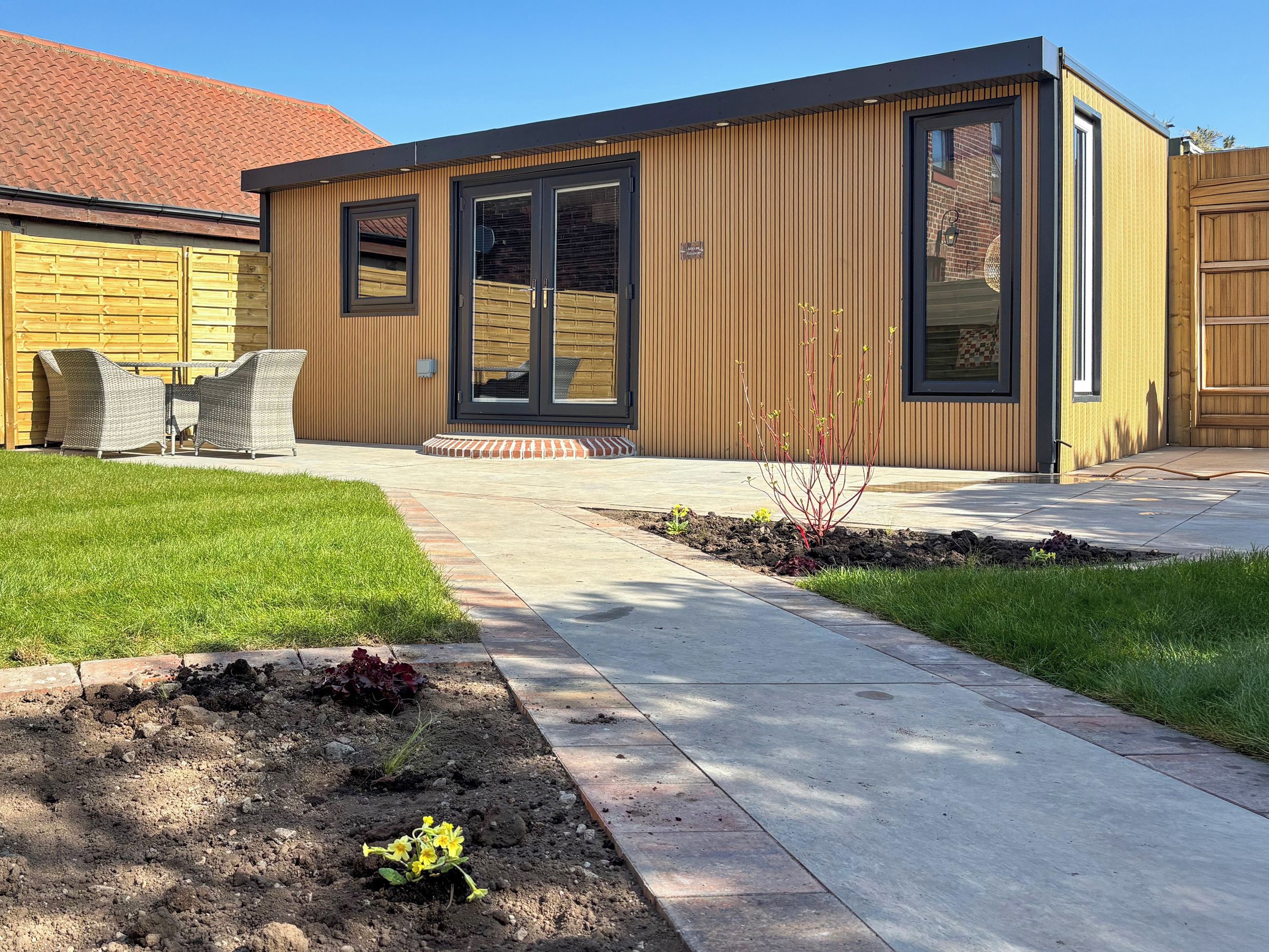 A modern building with a wooden exterior, a patio with outdoor furniture, and a well-maintained garden.