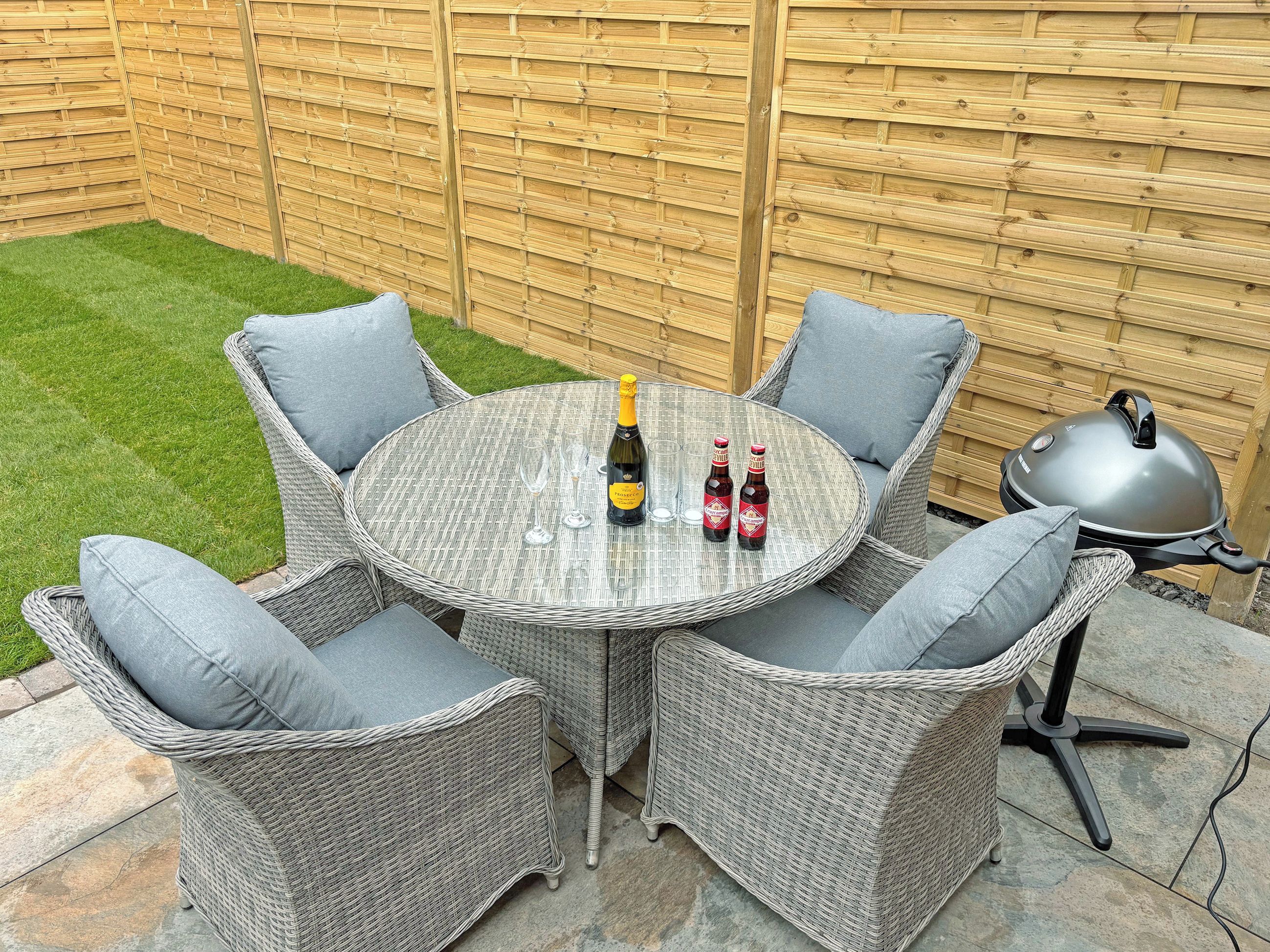 A round outdoor table with wicker chairs, a bottle of champagne, and two beer bottles.