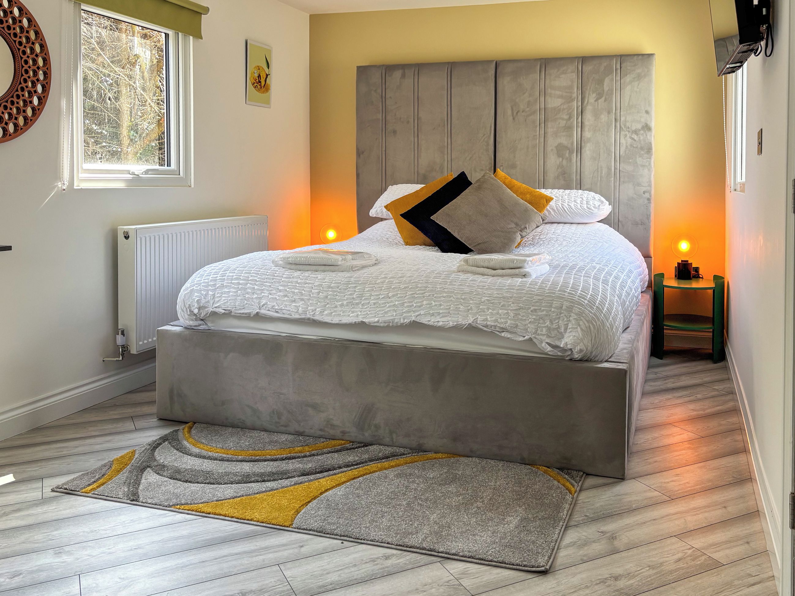 A bedroom with a bed, bedside table, radiator, and a window.