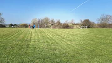 A grassy field with a playground and a goalpost.