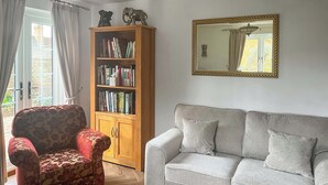 Een woonkamer met een gestreept fauteuil, een grijze bank, een houten boekenkast en een spiegel aan de muur.