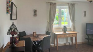 Een eethoek met een ronde tafel, stoelen, een lamp, een Boeddhabeeld en een televisie op een standaard.