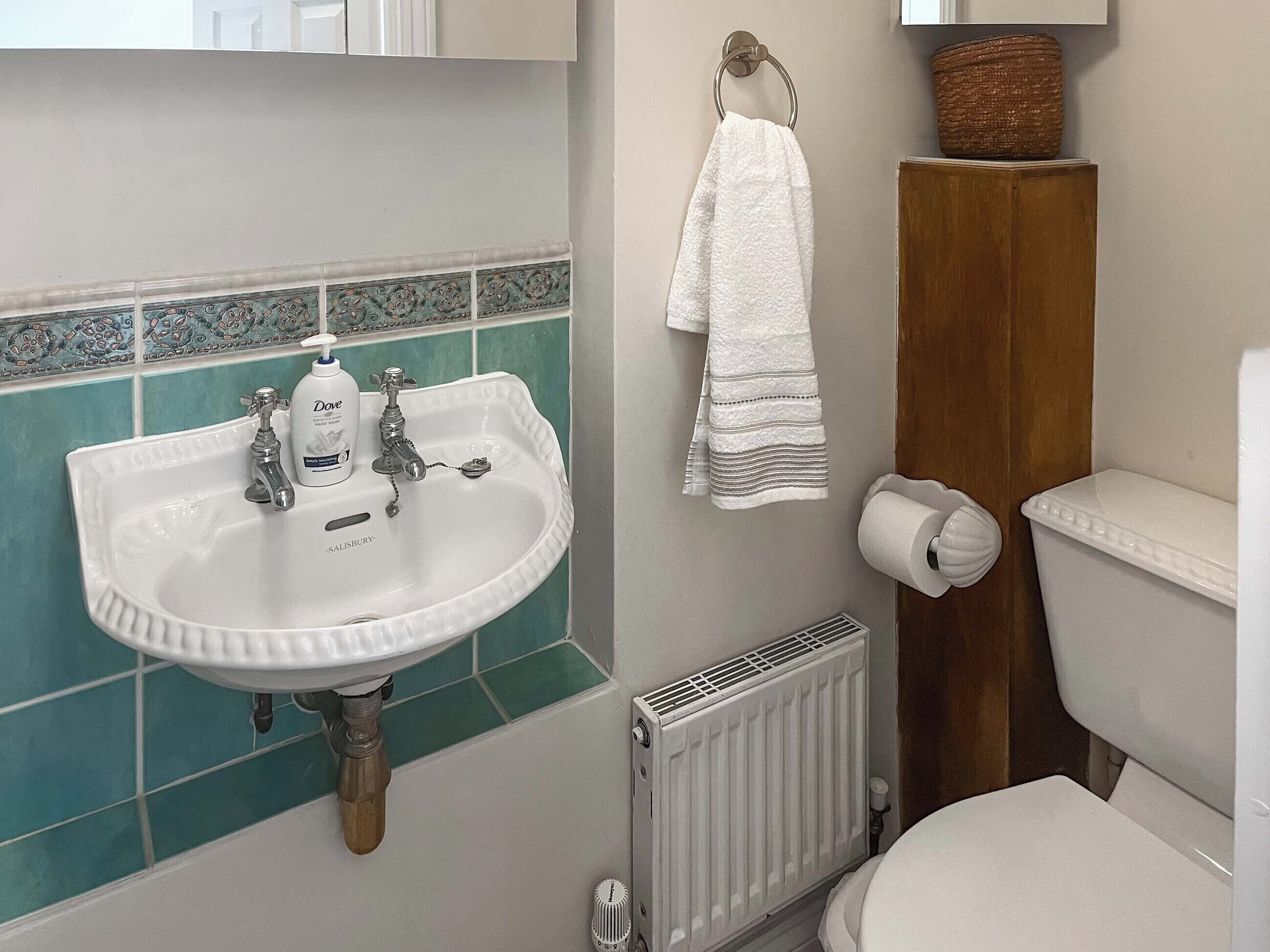 A bathroom with a white sink, a toilet, a towel rack, and a radiator.