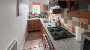 Een keuken met houten kastjes, een gasfornuis, een spoelbak en een raam met een rood vouwgordijn.