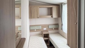 Ett kompakt inre utrymme i husbilen med två våningssängar, ett litet bord och ett fönster med gardiner.