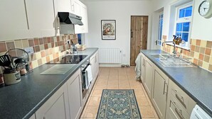 Une cuisine avec des armoires blanches, un comptoir noir, un pare-feu en carreaux, un tapis et une horloge au mur.