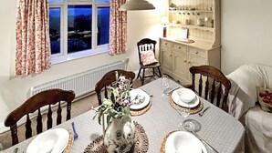 Une salle à manger avec une table dressée pour quatre personnes, des chaises, un vase rempli de fleurs et un buffet contenant de la vaisselle.