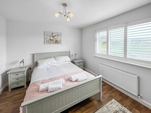 A bedroom with a bed, bedside tables, a radiator, a window with blinds, and a ceiling light fixture. - Magnolia Lodge - UK51603 (Sunset Lakes)