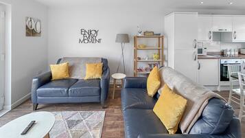 Een moderne woonkamer met twee banken, een salontafel, een boekenkast en een keukenhoek.