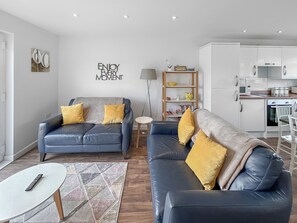 A modern living room with two sofas, a coffee table, a bookshelf, and a kitchen area.
