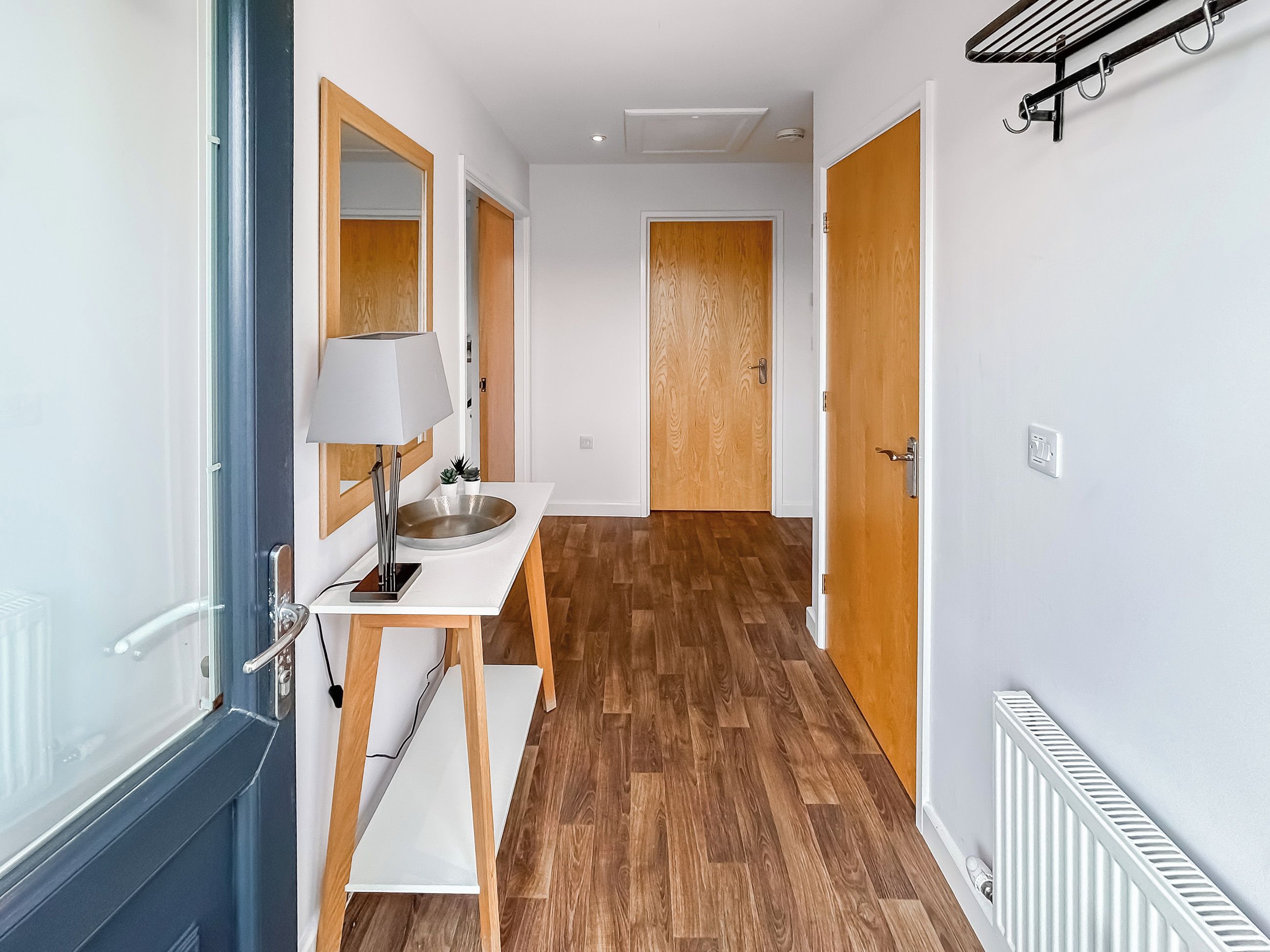 Un couloir étroit avec un plancher en bois, des murs blancs et un lavabo blanc surmonté d’un miroir.