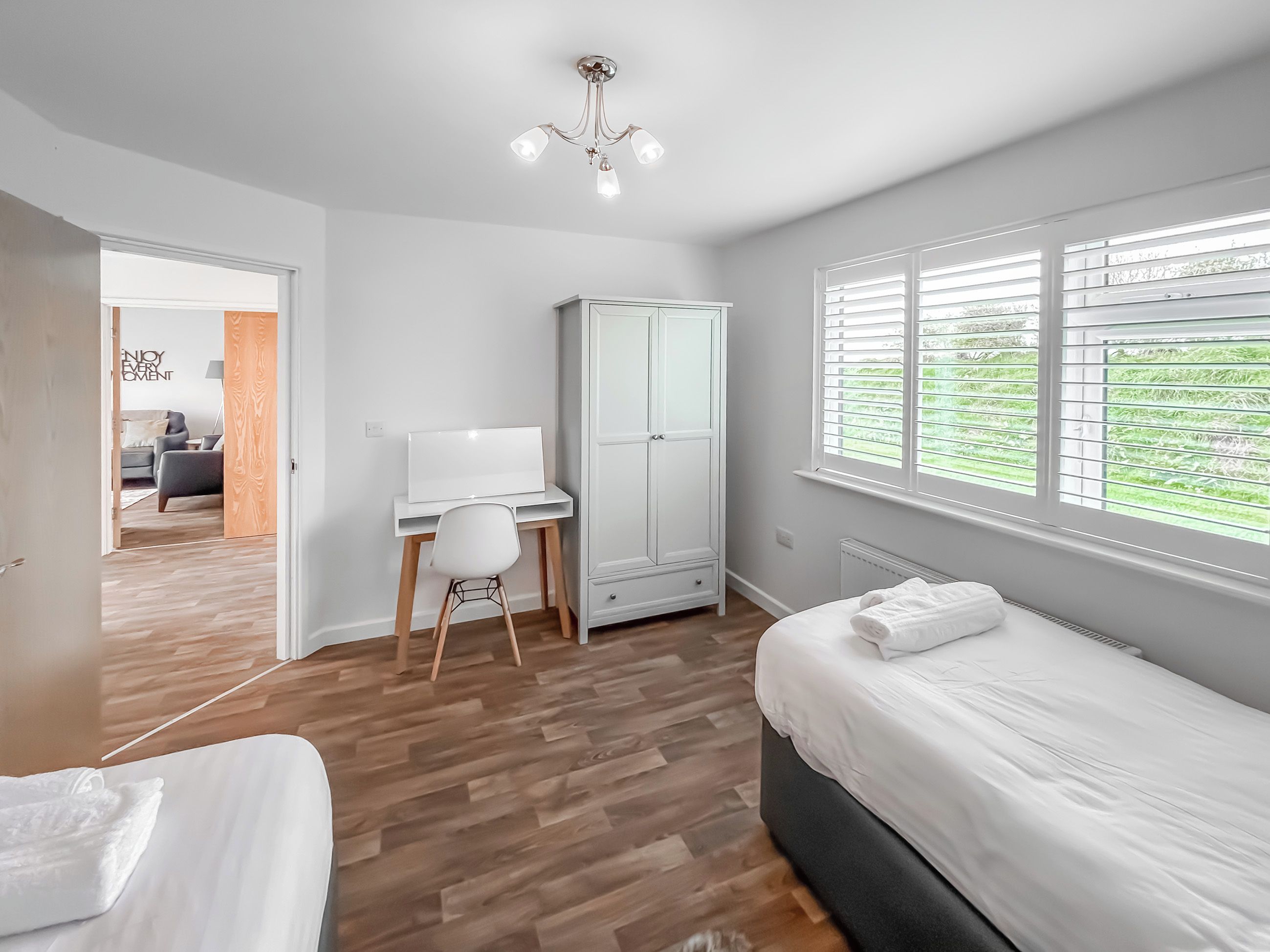 Een slaapkamer met een bed, een bureau, een stoel, een kledingkast en een raam met jaloezieën.