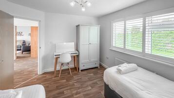Een slaapkamer met een bed, een bureau, een stoel, een kledingkast en een raam met jaloezieën.