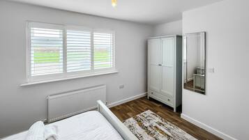 A bedroom with a bed, a radiator, a wardrobe, a mirror, and a window with blinds.