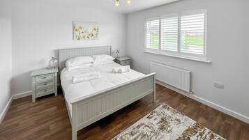 Une chambre à coucher comprenant un lit, des tables de chevet, un radiateur, une fenêtre avec des stores et un luminaire au plafond.