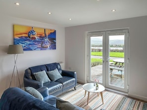 A living room with a sofa, a coffee table, a painting, and a sliding glass door leading to an outdoor area. - Wisteria Lodge - UK51605 (Sunset Lakes)