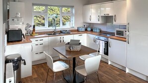 Una cocina moderna con armarios blancos, encimera de madera, un lavabo, un tostador, un hervidor y una ventana con vista a zonas verdes.