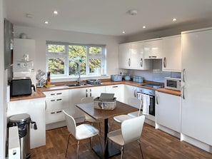 A modern kitchen with white cabinets, a wooden countertop, a sink, a toaster, a kettle, and a window with a view of greenery. - Wisteria Lodge - UK51605 (Sunset Lakes)
