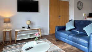 Una sala de estar con televisión, puerta de madera, reloj, sofá, lámpara, un globo terráqueo y control remoto.