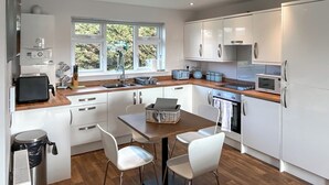 Une cuisine moderne avec des meubles blancs, un plan de travail en bois, un évier, un grille-pain, une bouilloire et une fenêtre donnant sur un paysage verdoyant.