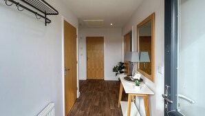 Un couloir avec un plancher en bois, un radiateur blanc, une porte, une table avec une lampe et un miroir.